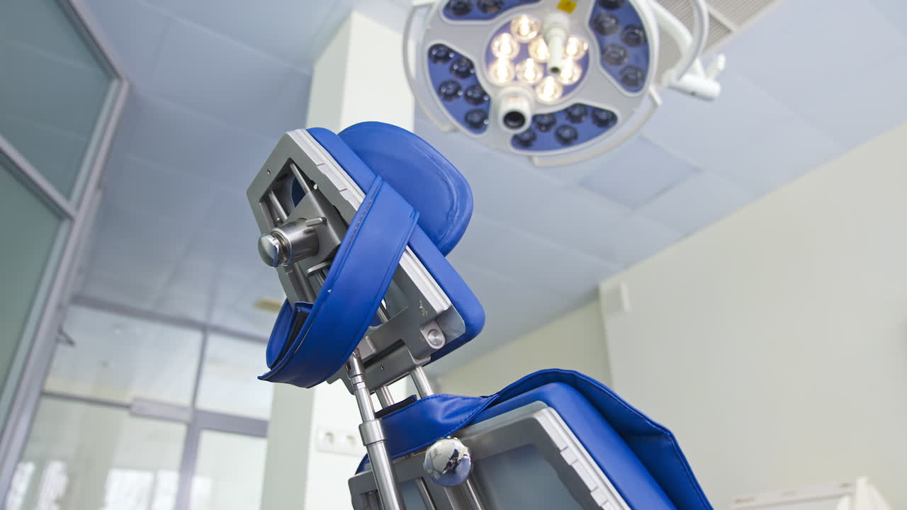 Folding chair with different appliances standing under the powerful lamp in dentist's cabinet. Close up. Low angle view. Blurred backdrop.