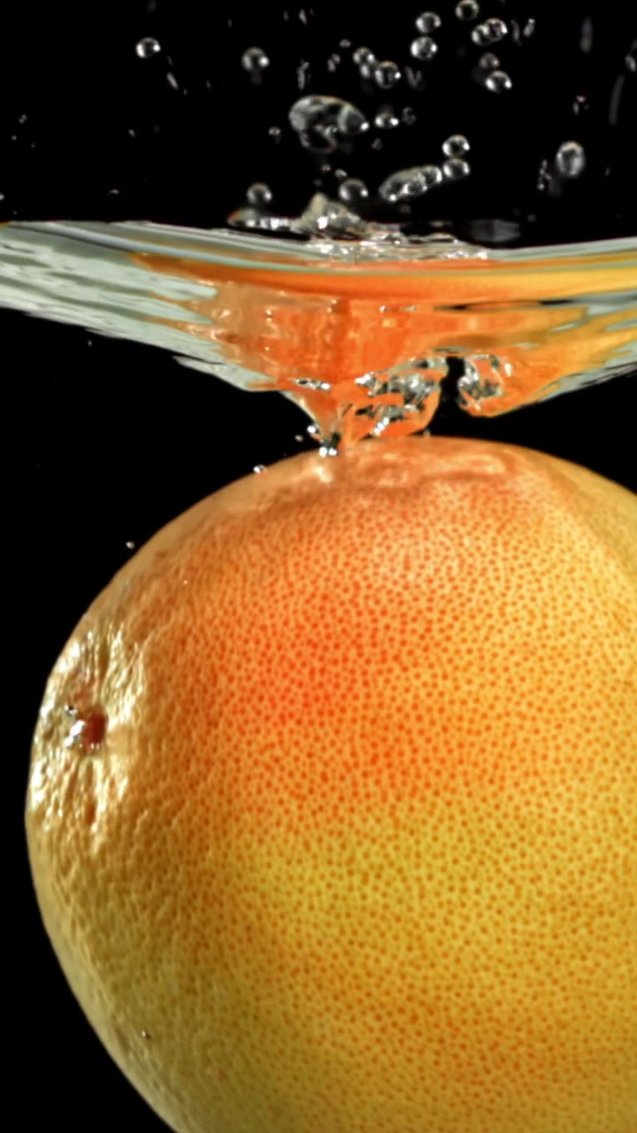 Pompelmo fresco che schizza nell'acqua su sfondo nero