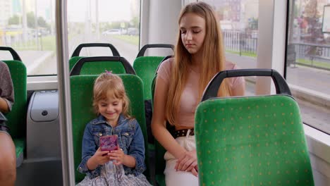 Tired-sleepy-woman-with-daughter-going-home-by-bus-after-hard-work-day,-child-kid-play-on-smartphone