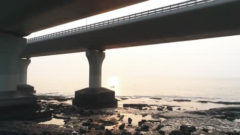 fly by under the bandra worli sea link, revealing a fisherman in a boat with the sun setting in the back