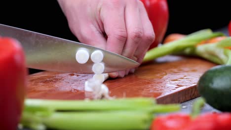 la cebolla de primavera se corta con un cuchillo en una tabla de cortar de madera rodeada de varias verduras