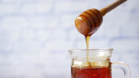 honey dripping from wooden dipper into glass jar