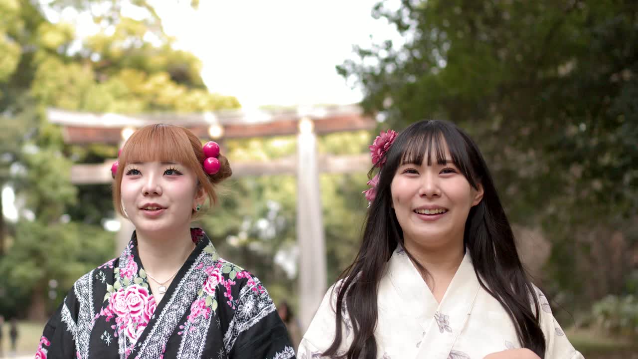 Due donne giapponesi che indossano yukata tradizionali camminano e parlano fuori dal cancello di un santuario shintoista.