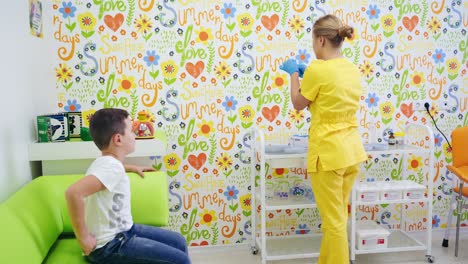 female doctor and child in the medical room. nurse in yellow uniform prepares syringe for injection. happy boy sitting in the armchair in clinic. health care concept.