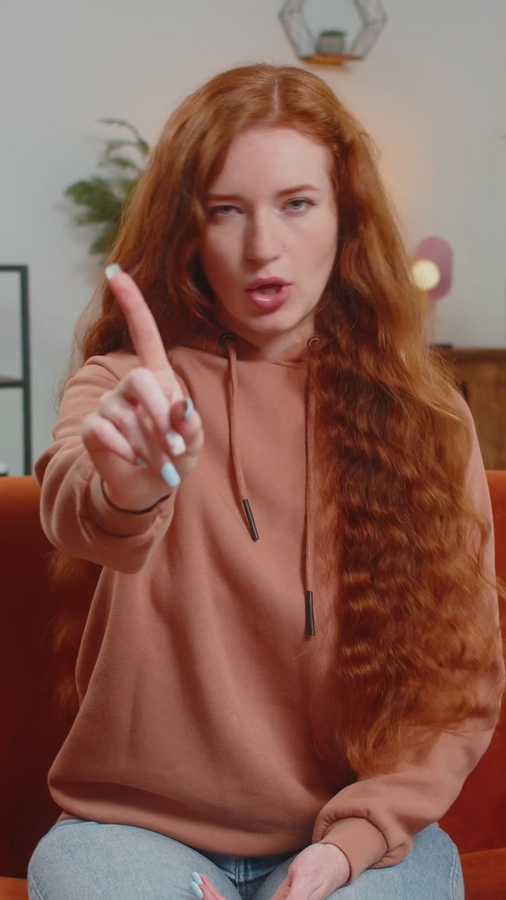 Displeased upset young woman sitting on sofa reacting to unpleasant awful idea shake finger no