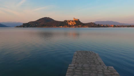 Escena-Pacífica-Del-Muelle-De-Hormigón-En-El-Lago-Maggiore-Aguas-Tranquilas-En-Italia,-Castillo-De-Angrya-En-El-Fondo