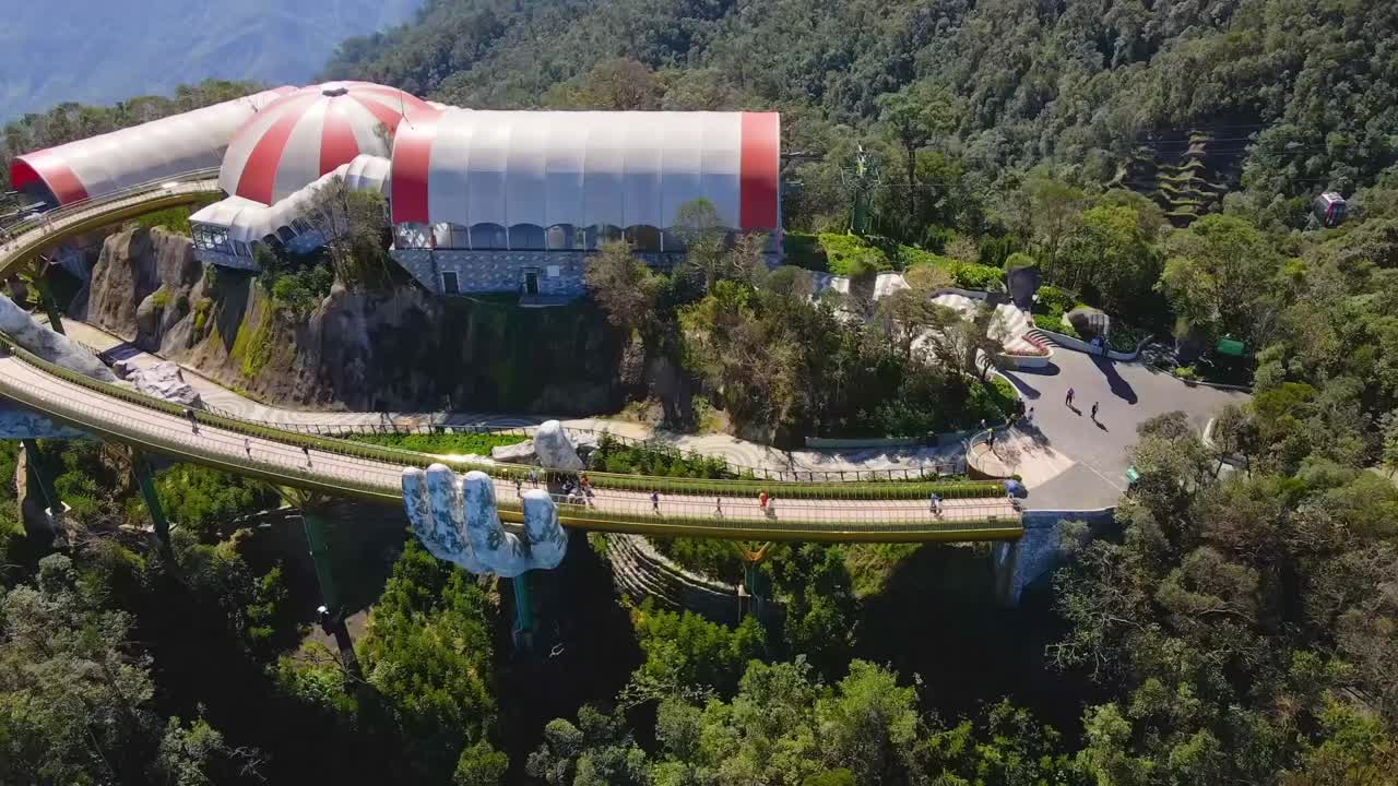 An aerial view of Vietnam’s Golden Bridge in Da Nang, gracefully held by giant stone hands amidst lush mountains, offering a unique architectural marvel in nature.