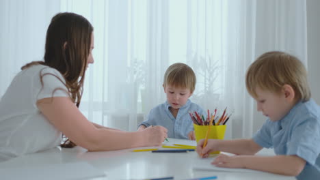 two children of boys draw with his mother sitting in the kitchen. happy family at home.