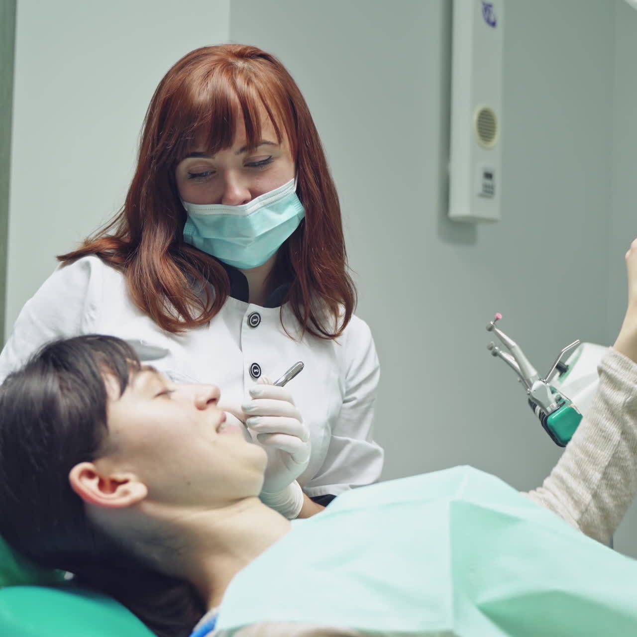 A dentist gives brunette a mirror for inspecting the result after the teeth whitening procedure at the stomatologic clinic.