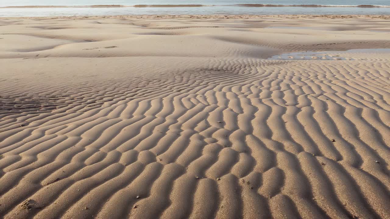 Câmera em movimento revelando ondulações na areia em uma planície de maré, mostrando uma poça de maré e seixos