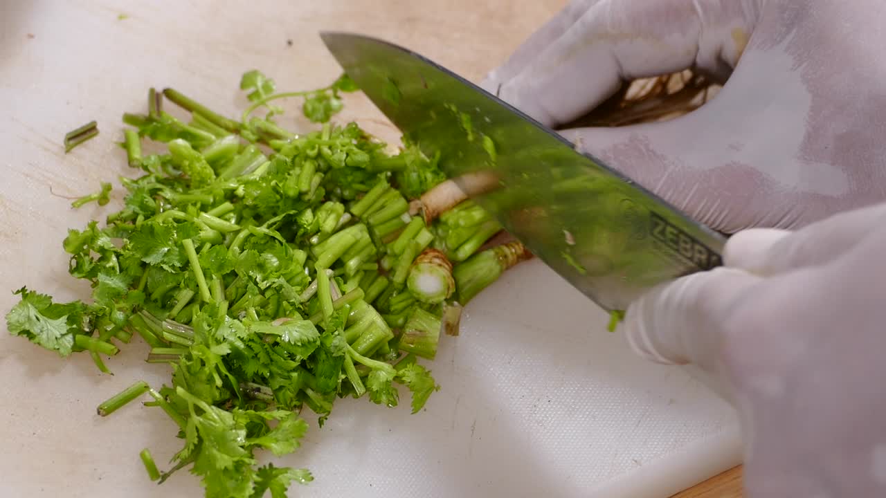 mano con guante cortando cilantro fresco en una tabla de cortar blanca, de cerca