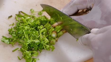 Mano-Con-Guante-Cortando-Cilantro-Fresco-En-Una-Tabla-De-Cortar-Blanca,-De-Cerca