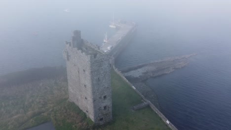 carrigaholt castle and fishing harbour in a summer seafog