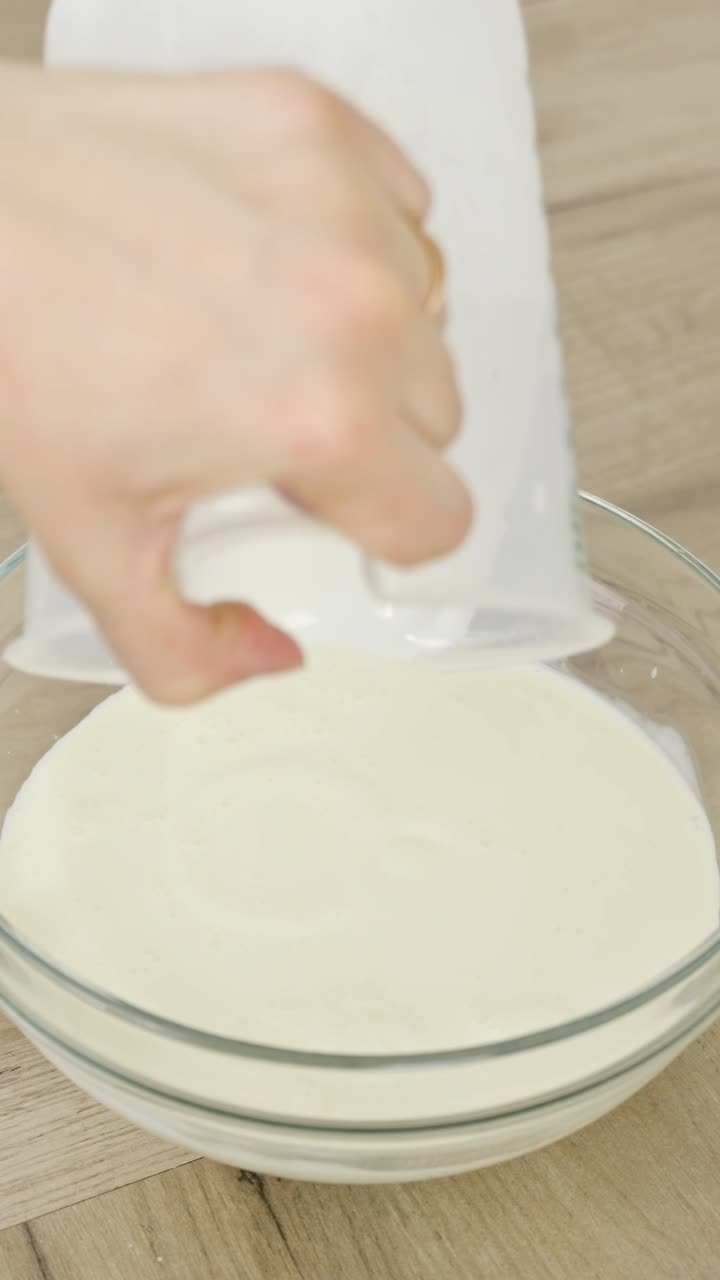 Vertical close-up of cream being poured into a glass bowl during tiramisu preparation.