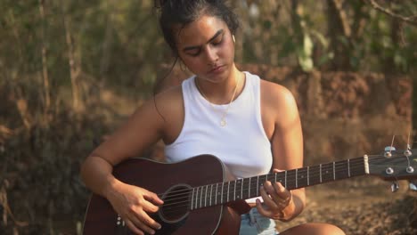 Close-up-slowmotion-shot-of-indian-girl-playing-the-guitar-during-sunset-with-a-tree-in-the-background