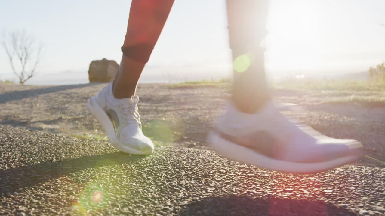 sección baja de mujer afroamericana haciendo ejercicio al aire libre corriendo en el campo durante el atardecer