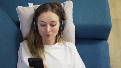 top view serene caucasian blonde woman lying on sofa pillow listening to music in headphones