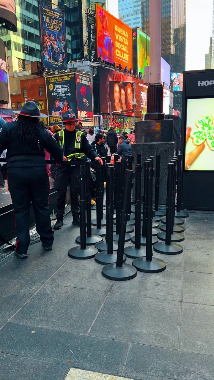 New York, USA, 22 March 2026: Uniformed security officers near digital display in Times Square. Group of officers standing by black stanchions and digital billboard showing clover leaf