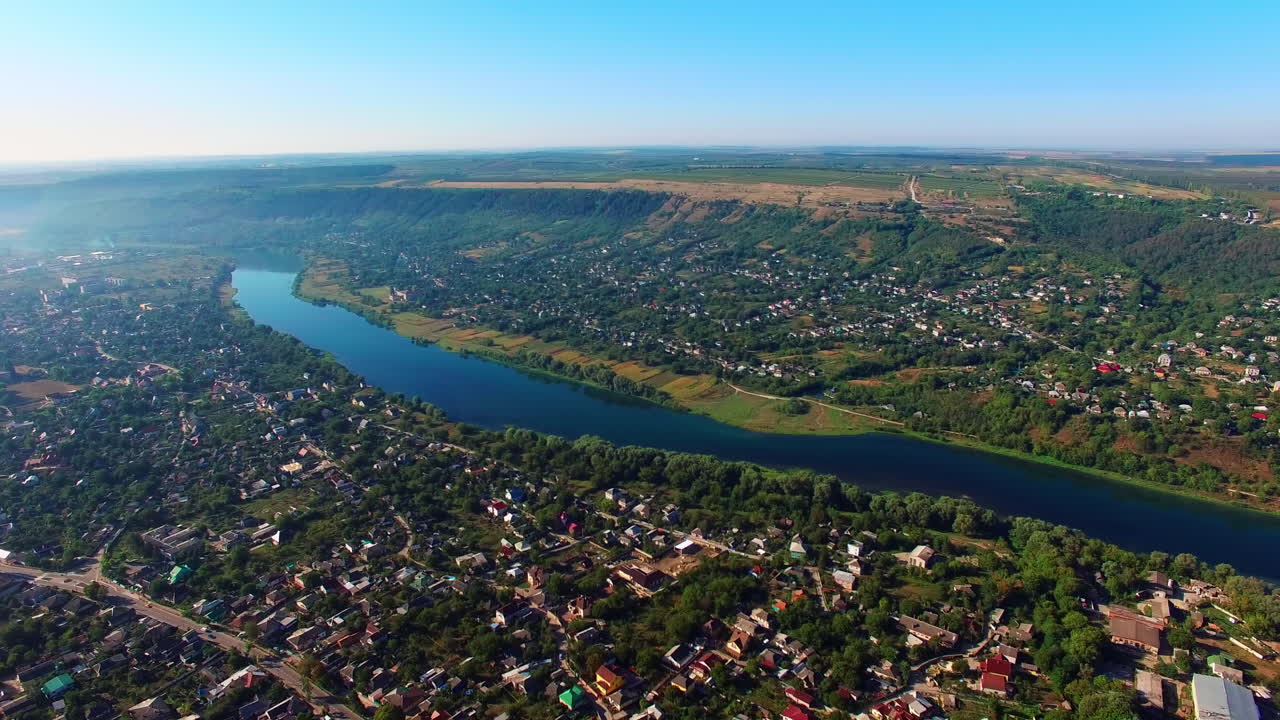 Picturesque city with narrow river dividing it into two banks. Urban landscape at sunny daytime from top. Hazy horizon at backdrop.