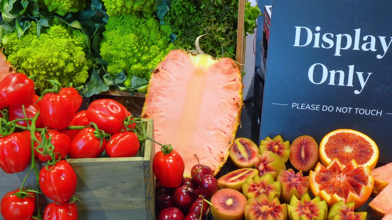 Exposição de produtos frescos com abacaxi e tomates, Chicago, Illinois. Vista em close-up de um abacaxi rosa fatiado, tomates cereja vermelhos, laranjas sanguíneas e brócolis romanesco verde sob luz interna brilhante.