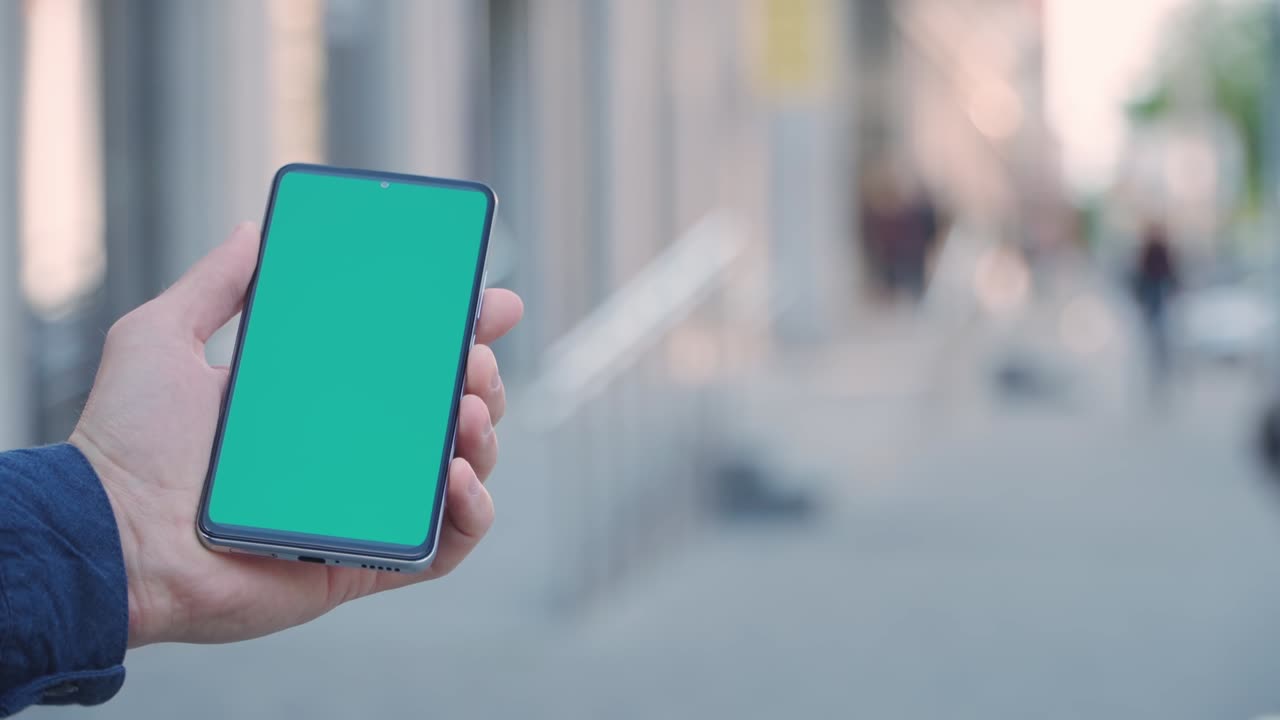 close-up de 4k de la mano de un hombre sosteniendo un teléfono inteligente con pantalla verde en una calle de la ciudad