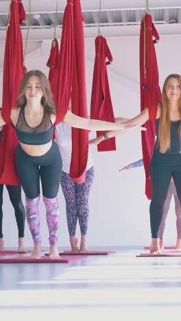 pretty slim ladies group enjoys practicing anti-gravity yoga asana with long red hammocks holding arms open