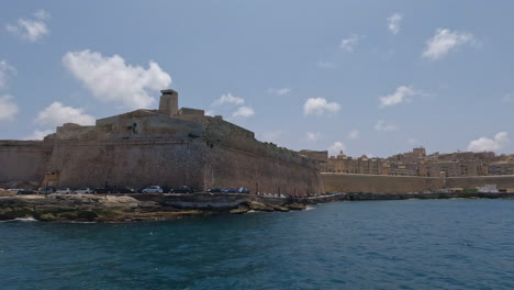 Boat-tour-off-the-coast-of-Malta,-Valletta-overlooking-pier-with-historical-building