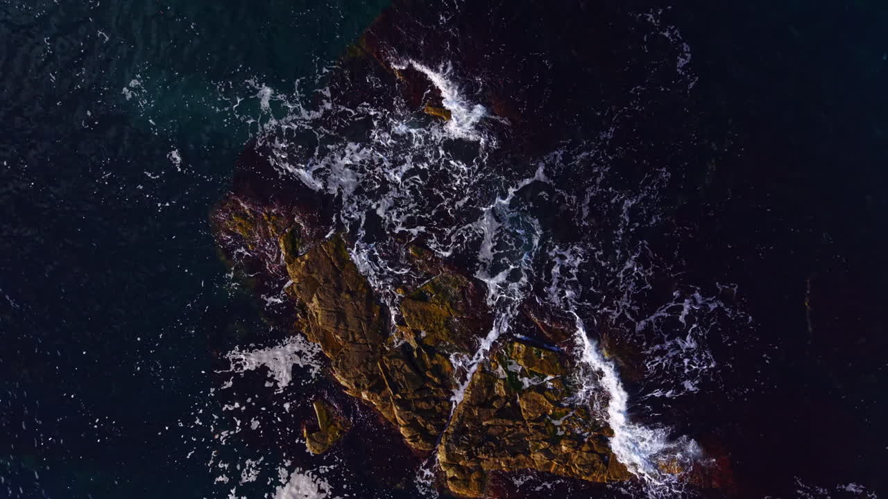 Waves crash against rugged rocks at twilight as nature's beauty unfolds in a serene coastal landscape