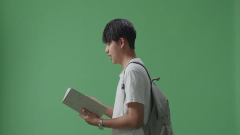 side view of asian man student reading book and walking on green screen studio