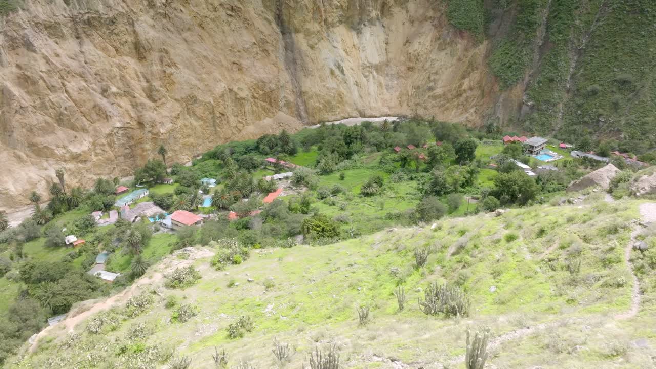 Close-up drone shot from the midway point of the descent, revealing the winding path toward Sangalle, surrounded by the dramatic cliffs of Colca Canyon and the lush oasis in the distance.