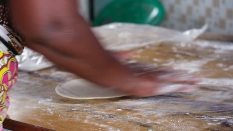 hands rolling dough with a wooden pin, preparing kenyan chapati on a floured surface