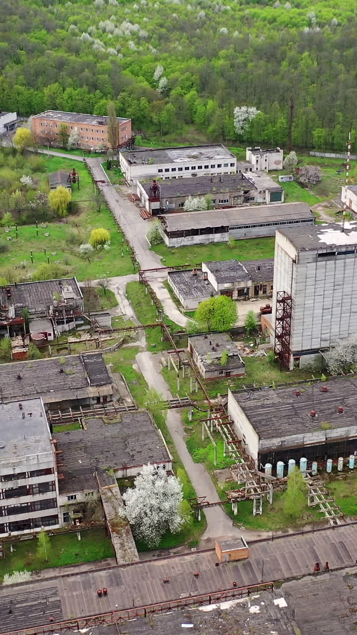 Abandoned factory industrial zone. Old factory warehouses. Ruined buildings on green nature background. Aerial drone view. Vertical video