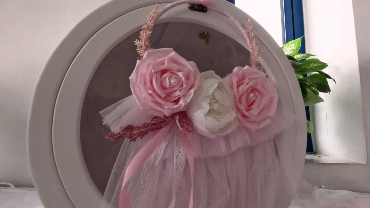 Una persona sta creando una decorazione floreale usando rose rosa e bianche per una festa. La stanza luminosa ha una finestra con luce naturale. Questo progetto prevede semplici passaggi e strumenti di crafting.