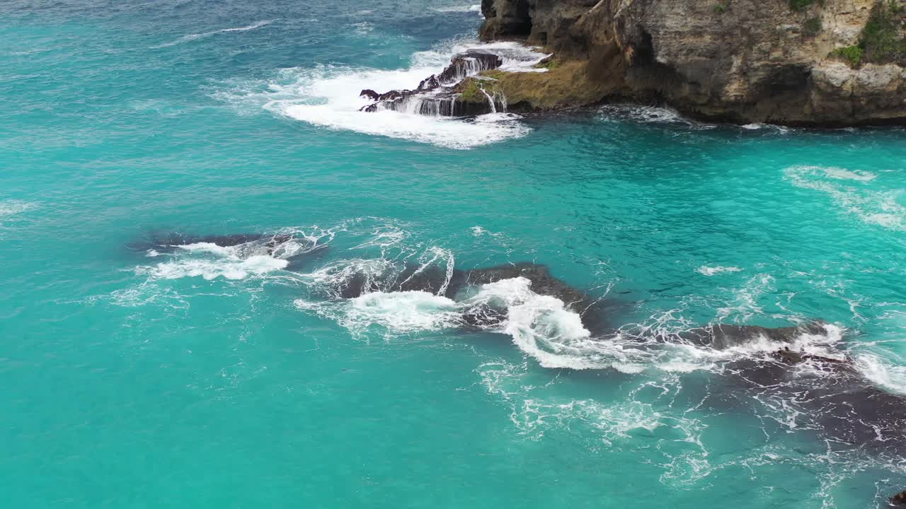 Acqua tropicale turchese che si infrange su rocce frastagliate alla Laguna Blu sull'isola di Nusa Ceningan, vista aerea