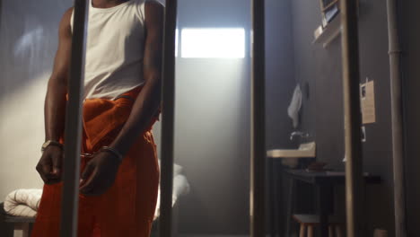 handcuffed african american inmate walking behind prison cell bars