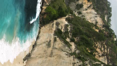 inclinación vertical tomada frente a los acantilados de nusa penida con vistas a la hermosa playa de diamantes mientras las olas del mar azul lavan en la playa