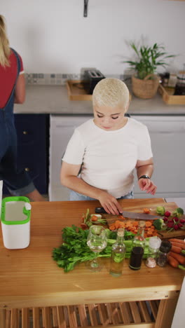 video vertical de una mujer biracial feliz cortando verduras en la cocina