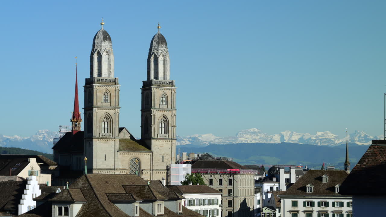 Static shot of Grossmünster facade on sunny day, Alps in background