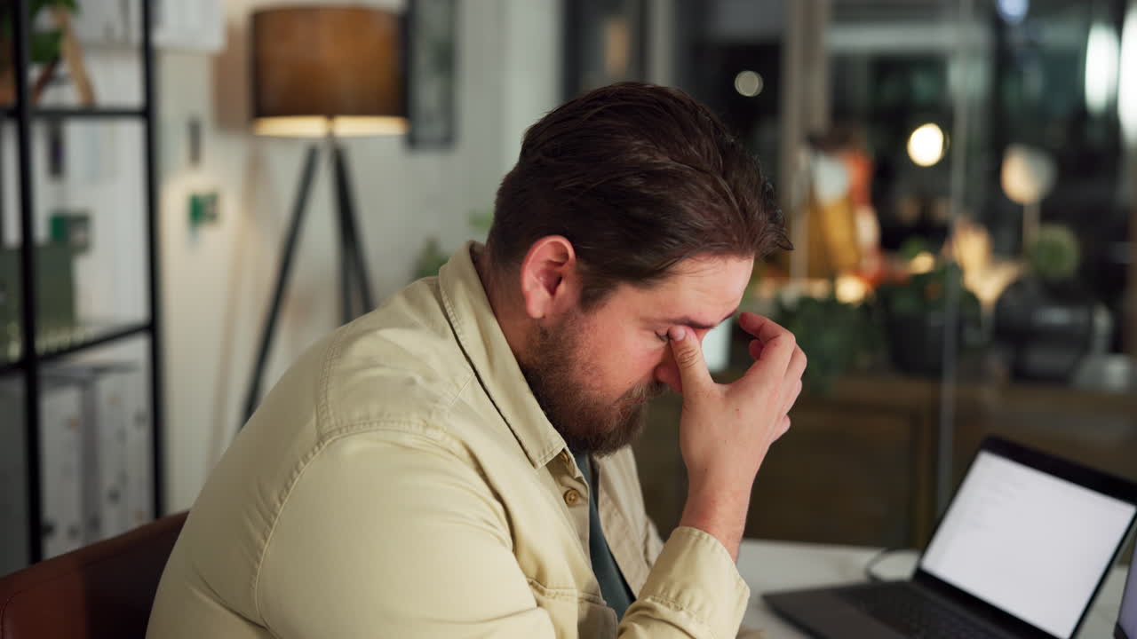 Un hombre cansado bosteza y se frota los ojos mientras trabaja en el portátil