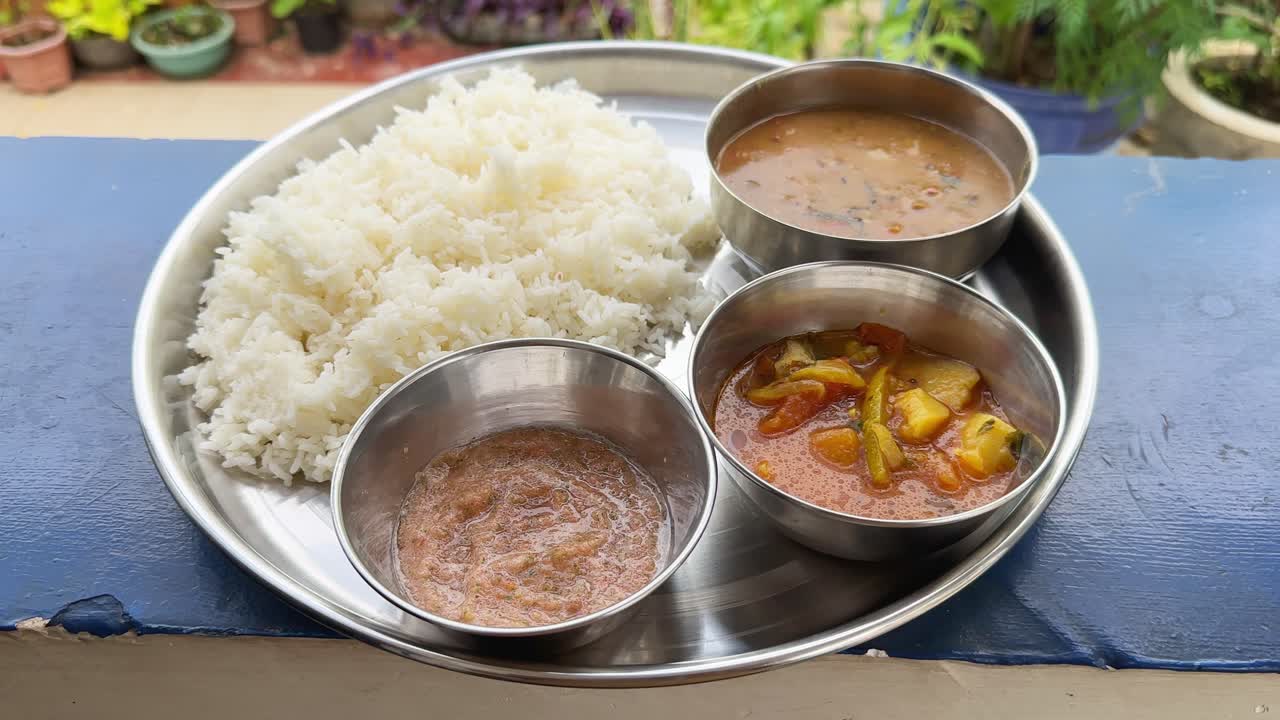 Tracking shot of A stainless steel plate serves up a traditional Indian meal: steaming rice, dal, vegetable curry, and chutney
