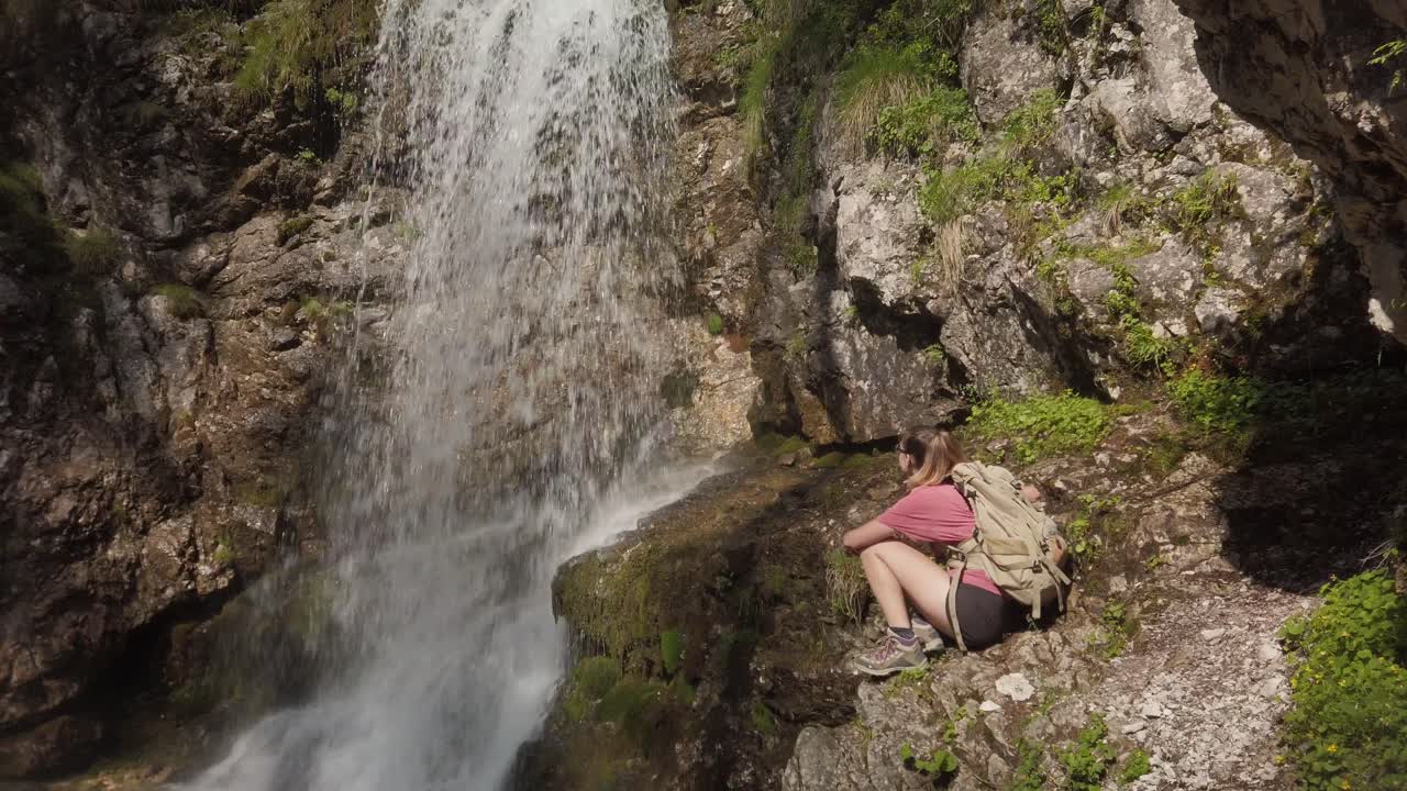una chica de excursión está sentada en una roca cerca de una cascada en una reserva natural