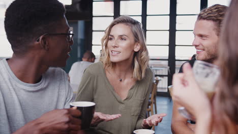 gruppe von freunden sitzt an einem tisch in einem geschäftigen café und unterhält sich