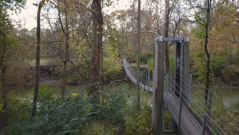 Drone-shot-of-a-suspension-bridge-in-the-middle-of-the-woods-above-a-river-during-the-autumn-season