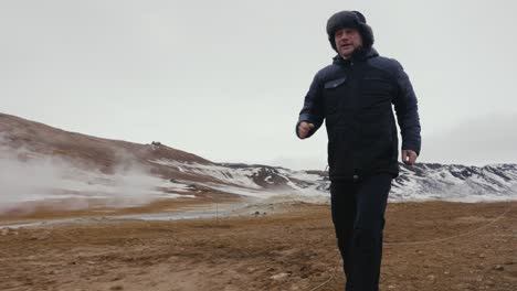 man run on myvatn geothermal area on dirt road, steam in background