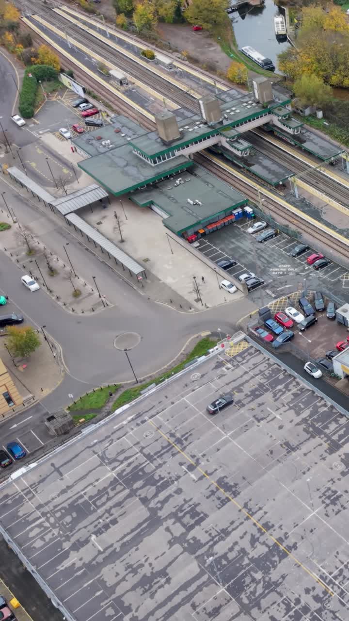 Vertical drone orbit over Harlow Town train station, capturing platforms, tracks, and local car park. Harlow Marina and canal boats are in the background, showing a complete aerial perspective