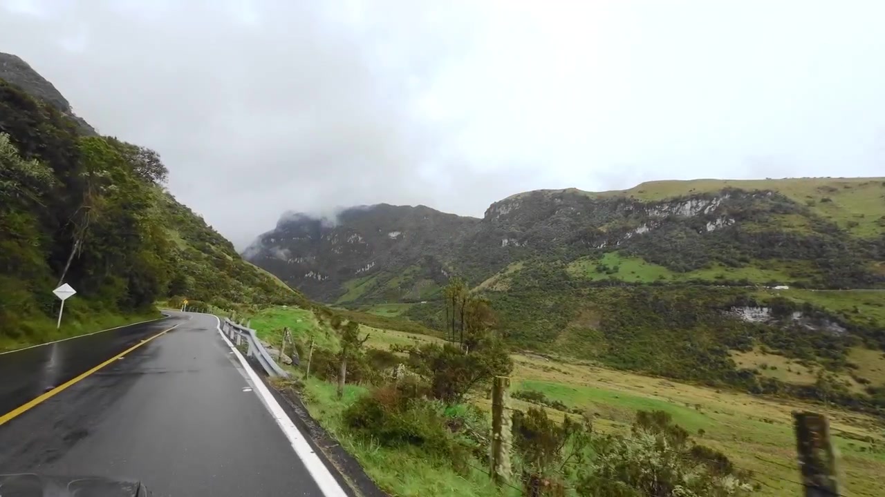 Una prospettiva dal veicolo che viaggia lungo la strada Murillo-Manizales accanto a un'ampia valle, con catene montuose andine stratificate che raggiungono l'orizzonte