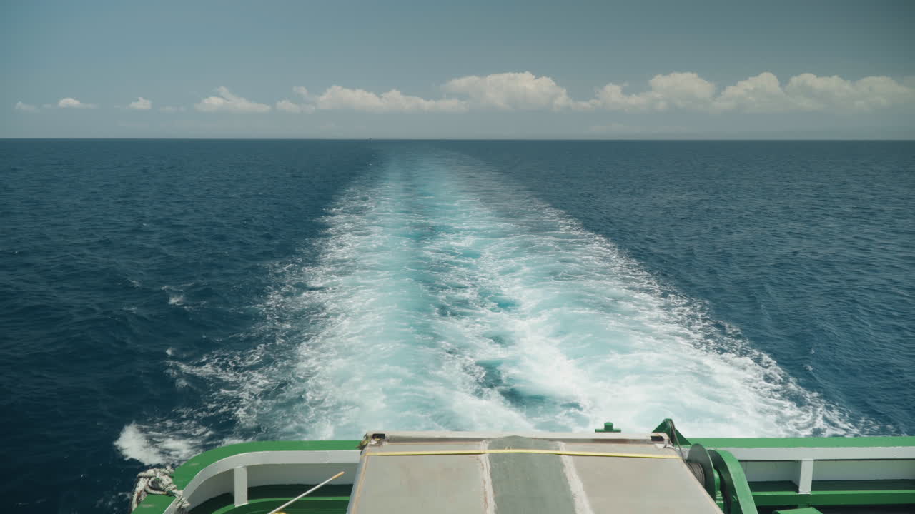 Heckwelle des Schiffes im tiefblauen Meer, Meereshorizont unter sanften Wolken, Heckreling sichtbar, aufgewühlte türkisfarbene Spur und weißer Schaum, Sonnenlicht glitzert auf den Wellen, ruhige, abenteuerliche Stimmung