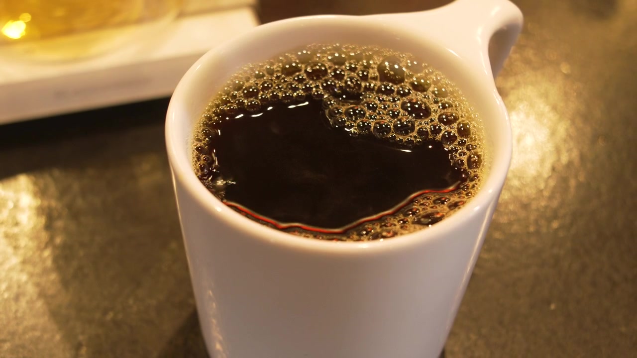 モダンなコーヒーバーで、白いマグカップに入った淹れたてのブラックコーヒーと芳醇な黄金色の泡。