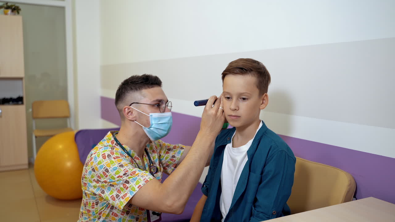Doctor Examining Boy Ear. Doctor auscultating the ear of child with otoscope in examination room