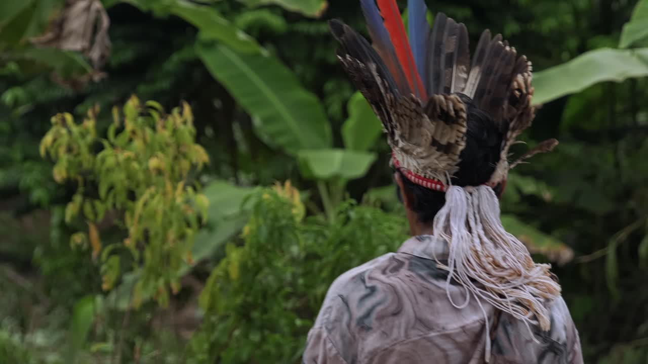 Following a tribal man wearing a feathered headdress and walking forward